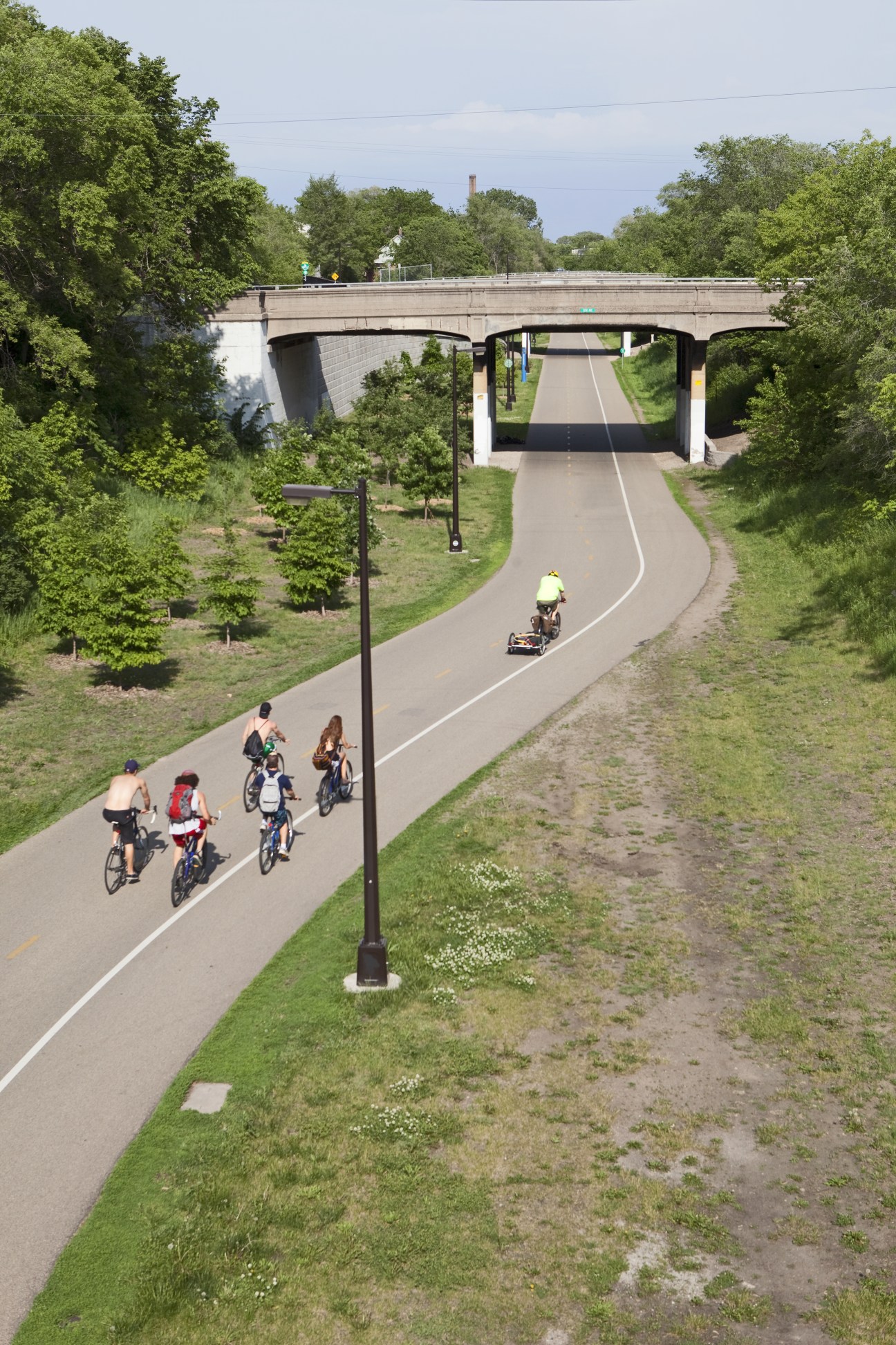 Cyclists and pedestrians on the Midtown Greenway bike trail under a concrete bridge along a converted rail corridor.
