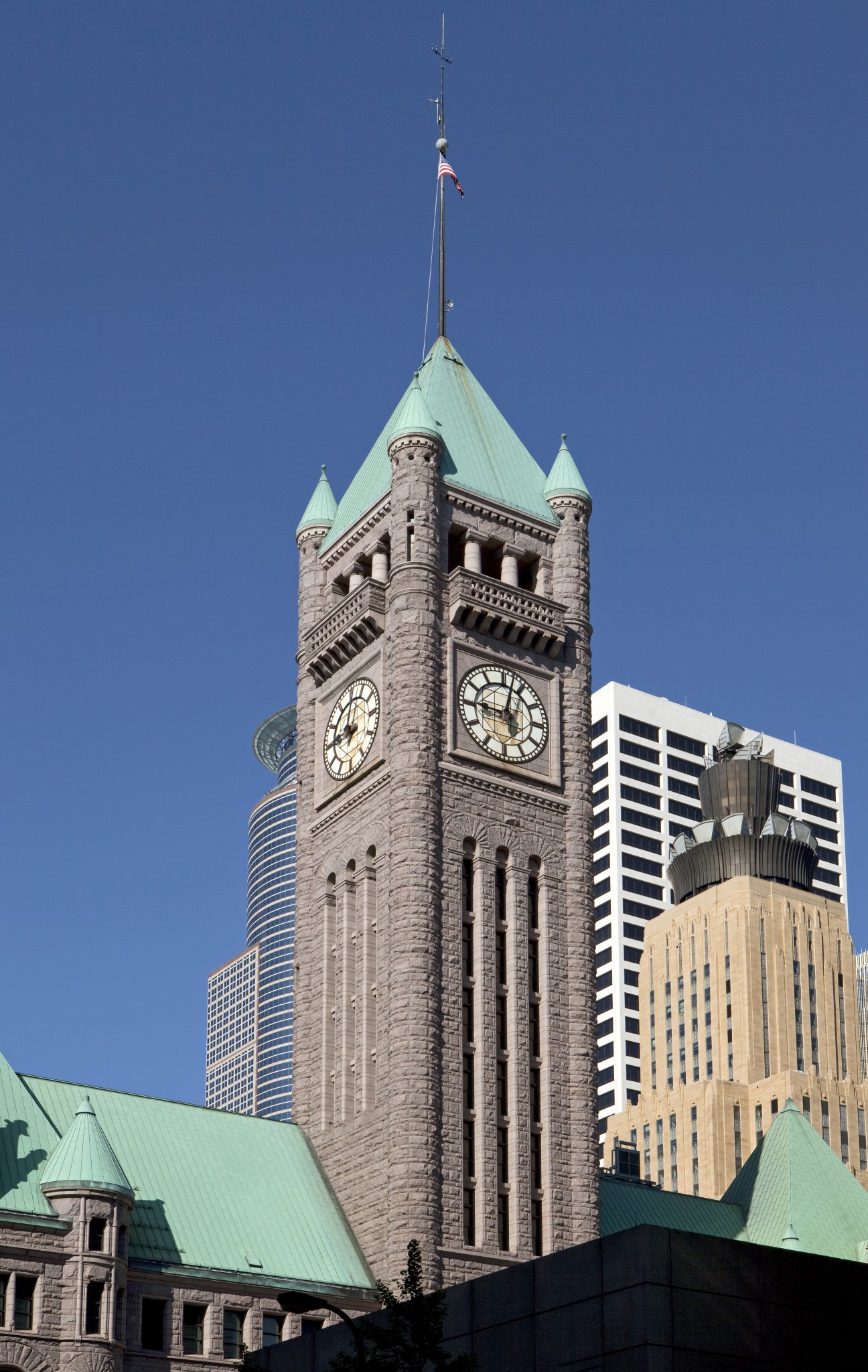 Minneapolis City Hall clock tower with green copper roof spires against blue sky and modern buildings.