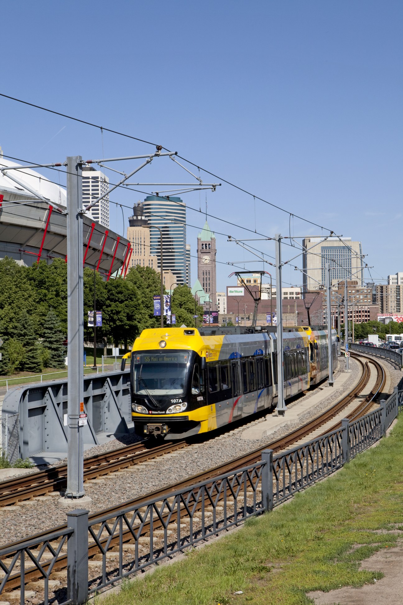 Yellow and blue light-rail train on tracks with Minneapolis skyline in background.