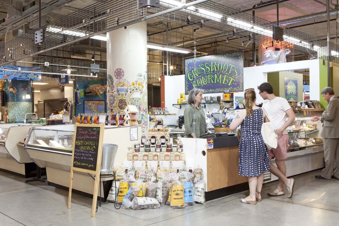 Grass Roots Gourmet vendor stall at Midtown Global Market with customers and displayed local products.