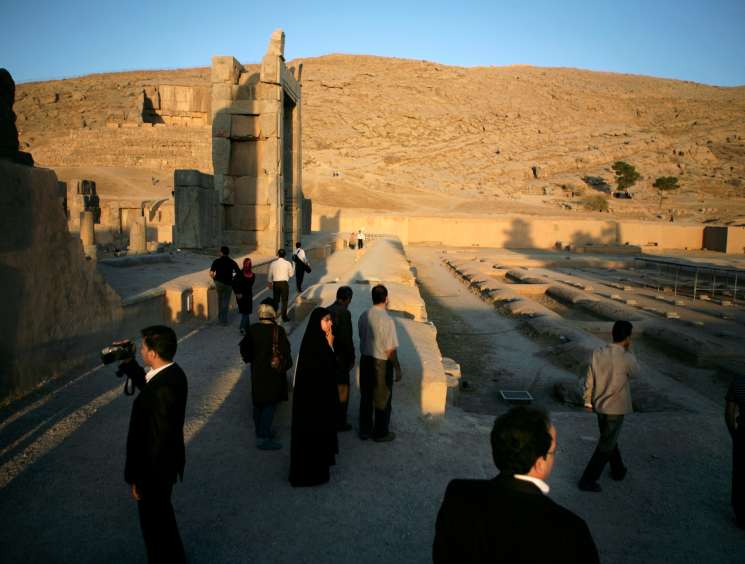 Tourists visit ancient Persian ruins at Persepolis with stone columns and desert landscape.