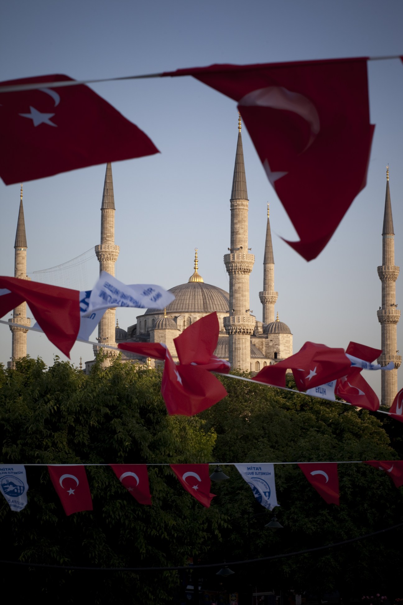 Turkish flags flutter in front of Istanbul mosques with minarets visible against a blue sky.
