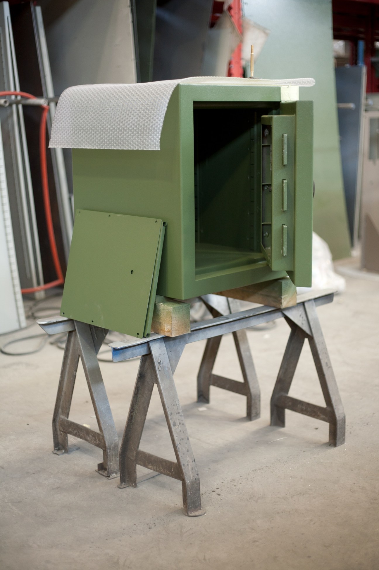 A green safe under construction mounted on metal sawhorses in a factory workshop.