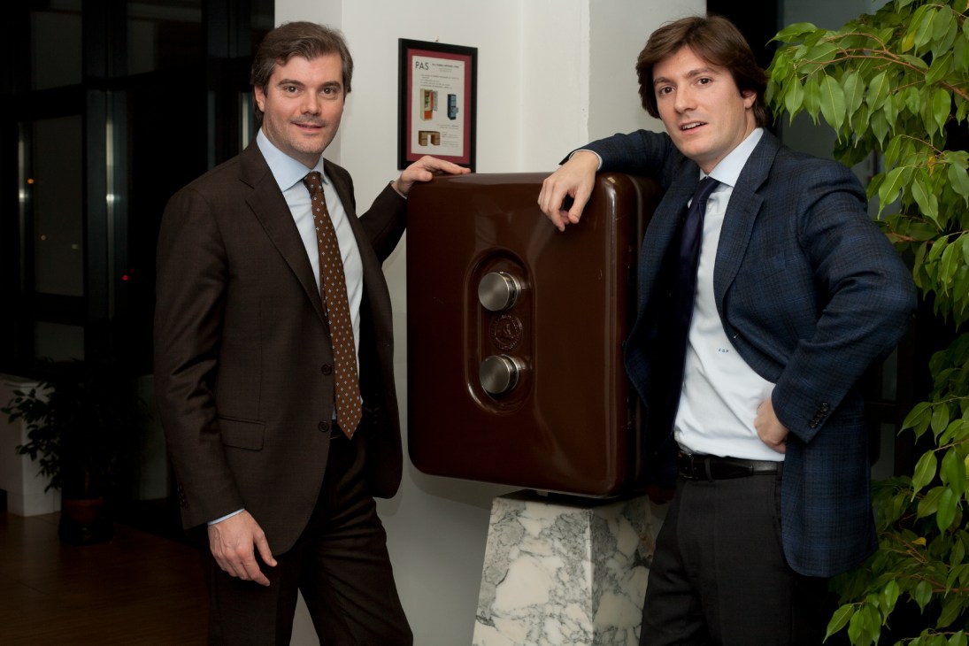 Brothers Alberto and Emanuele Parma pose with a brown wooden safe featuring two combination locks.