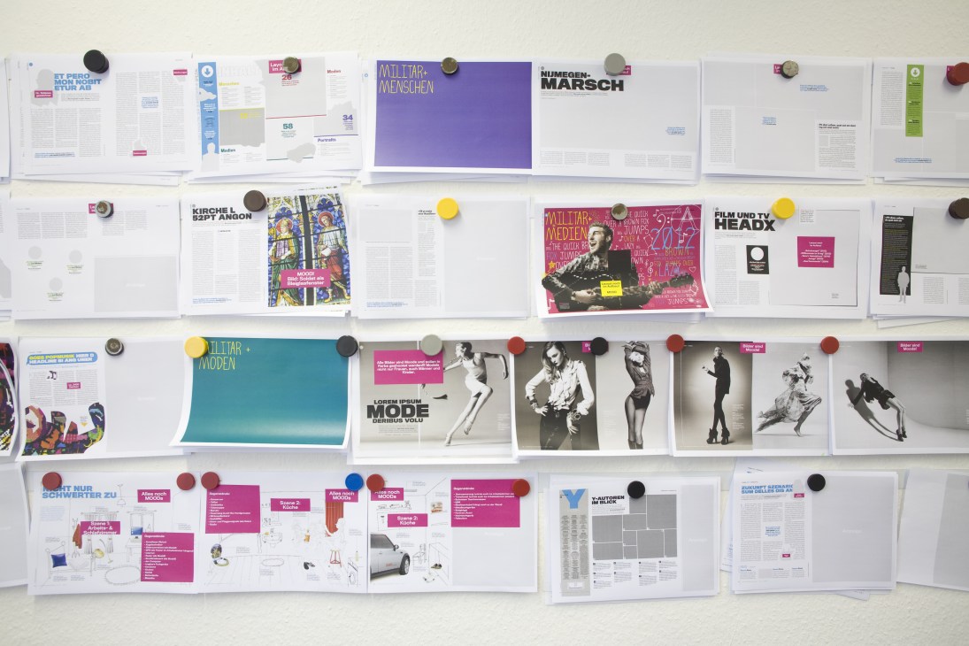 Magazine layout sheets and design mockups pinned to a wall during editorial planning.