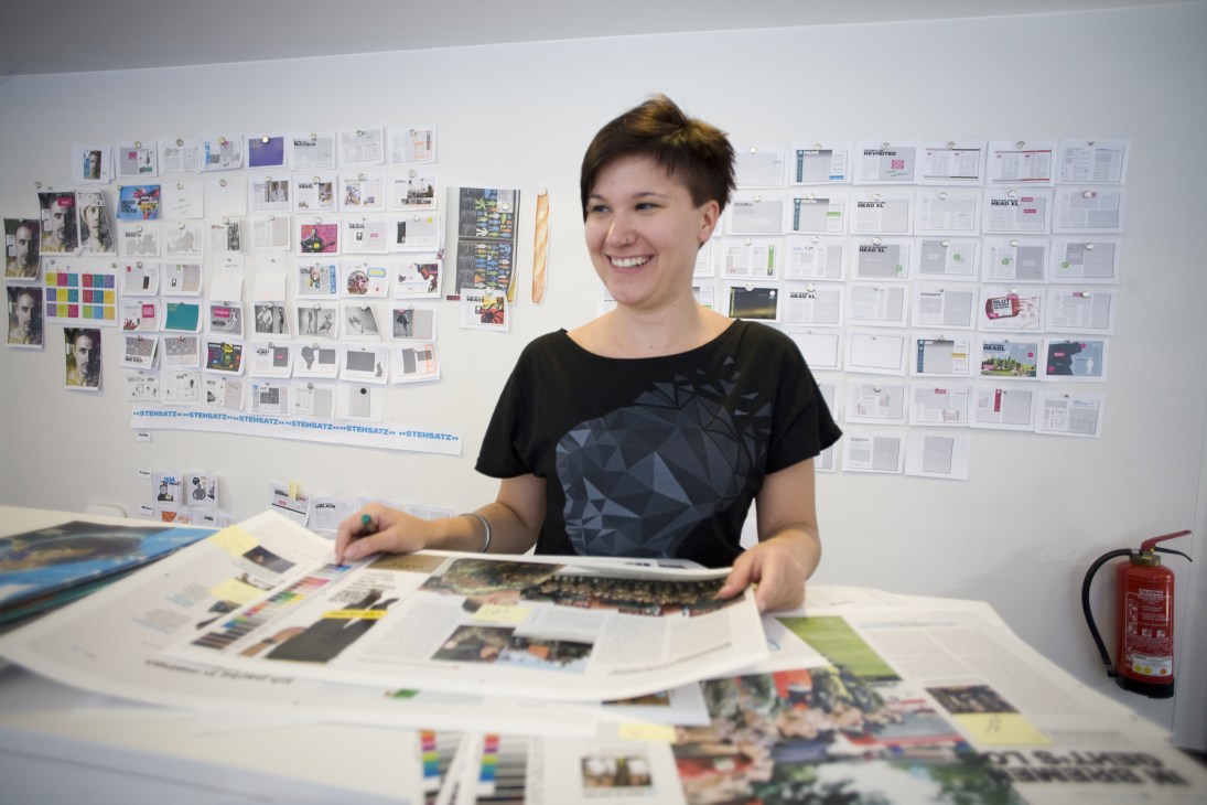 Junior art director Mareike Bongen smiles while working with magazine layouts and design samples at her desk.
