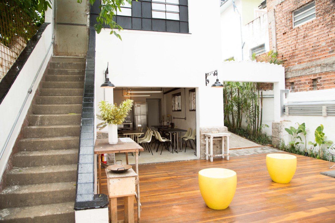 Guest Urban's São Paulo courtyard with wooden deck, yellow planters, and modern dining area opening onto the street.