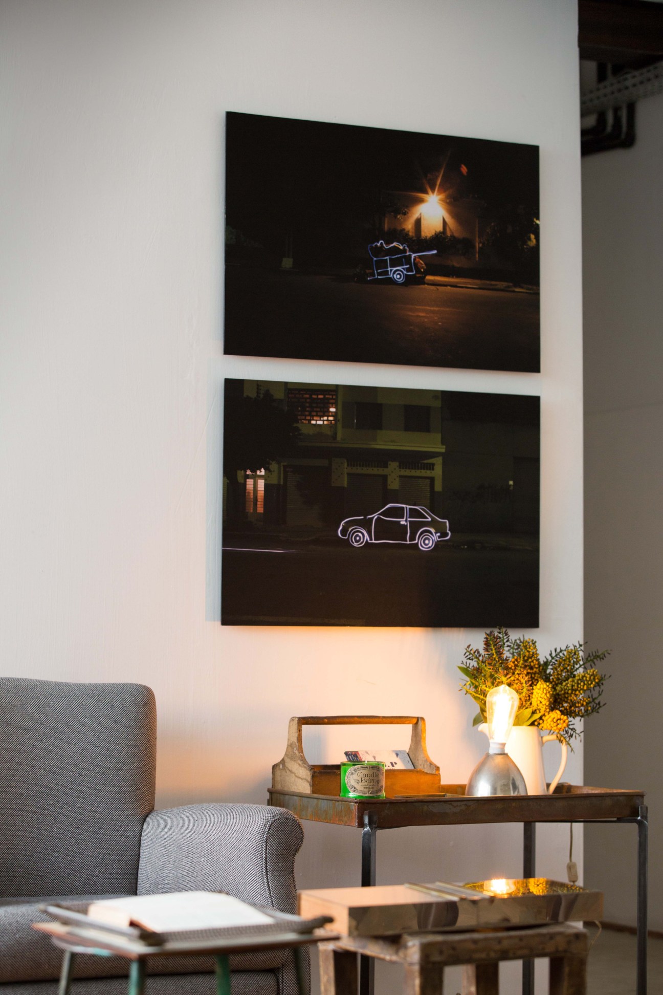 Modern living room with neon car and truck artwork on white wall above side table.