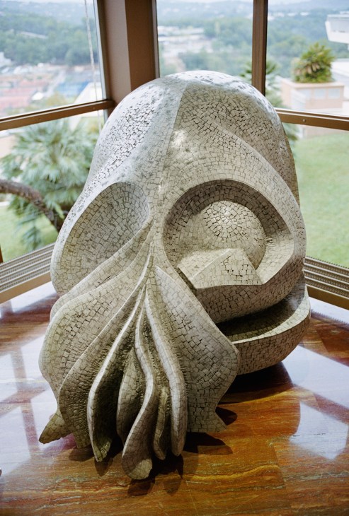 Stone sculpture by Gérard Brand displayed in a modern lobby with panoramic windows overlooking Sophia Antipolis landscape.