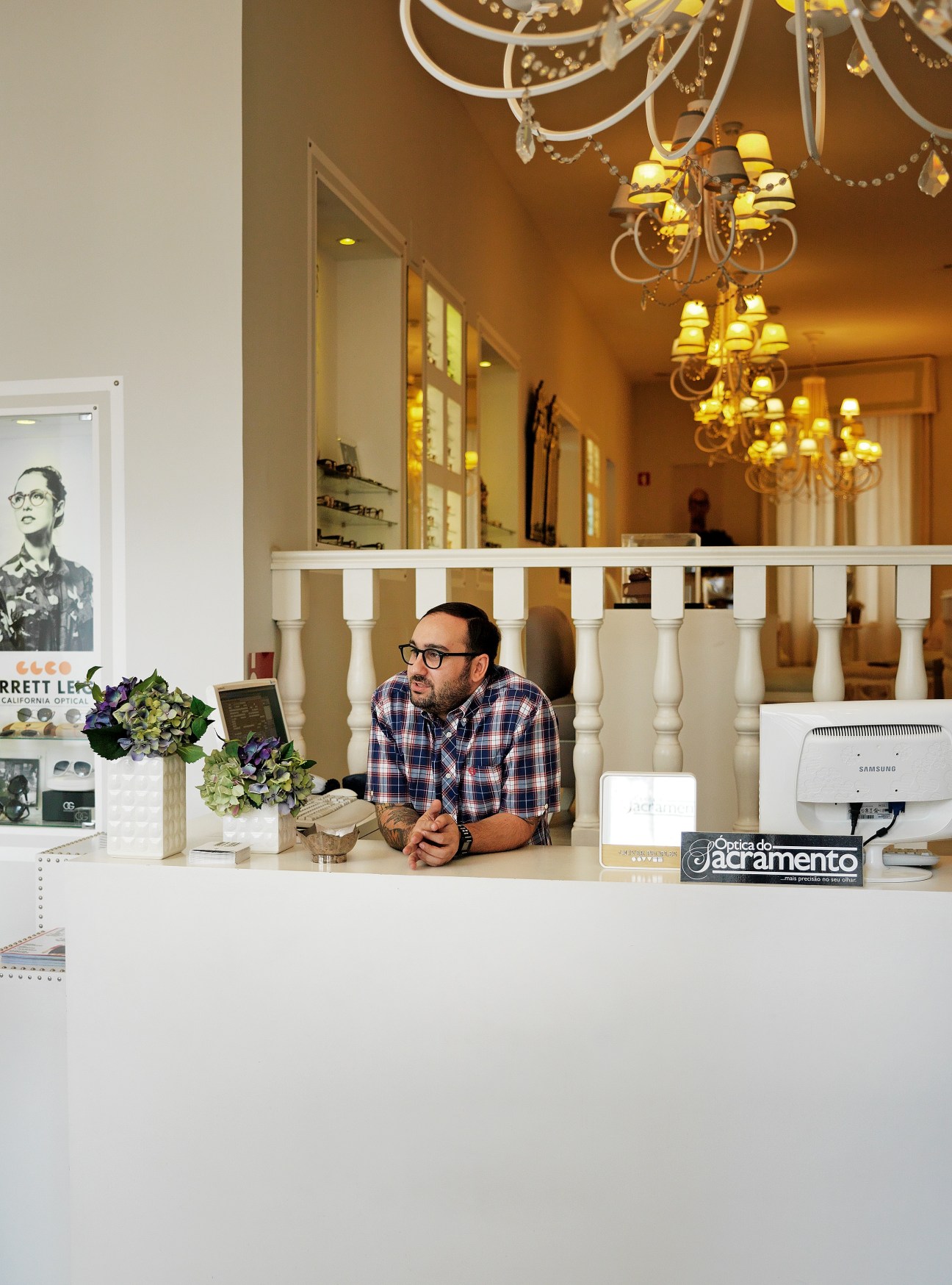 Optician Rui Romão stands behind the counter at Óptica Do Sacramento, an elegant eyewear shop with chandeliers and formal dining room-like décor.