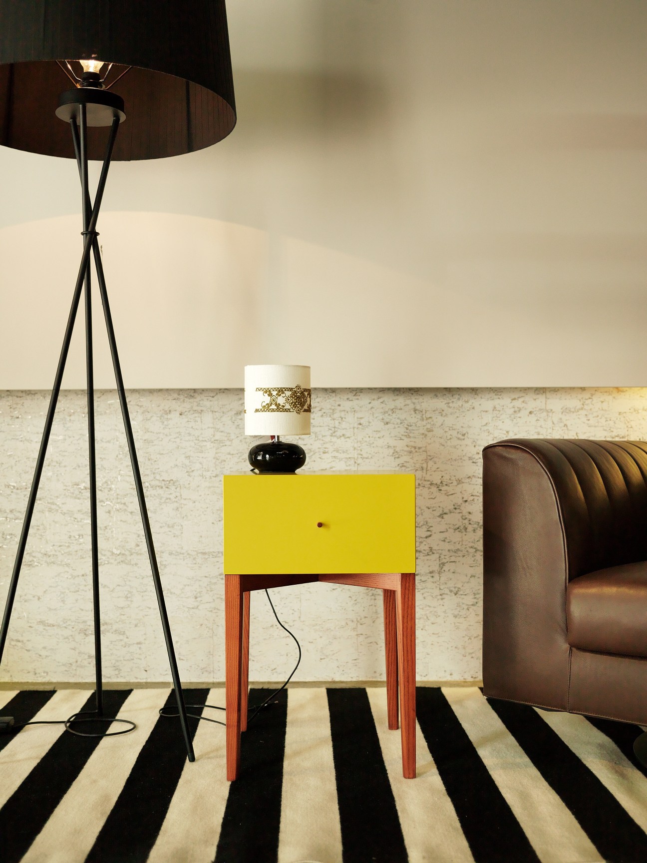 Modern interior at Espaço Mínimo with yellow side table, tripod floor lamp, and leather chair.