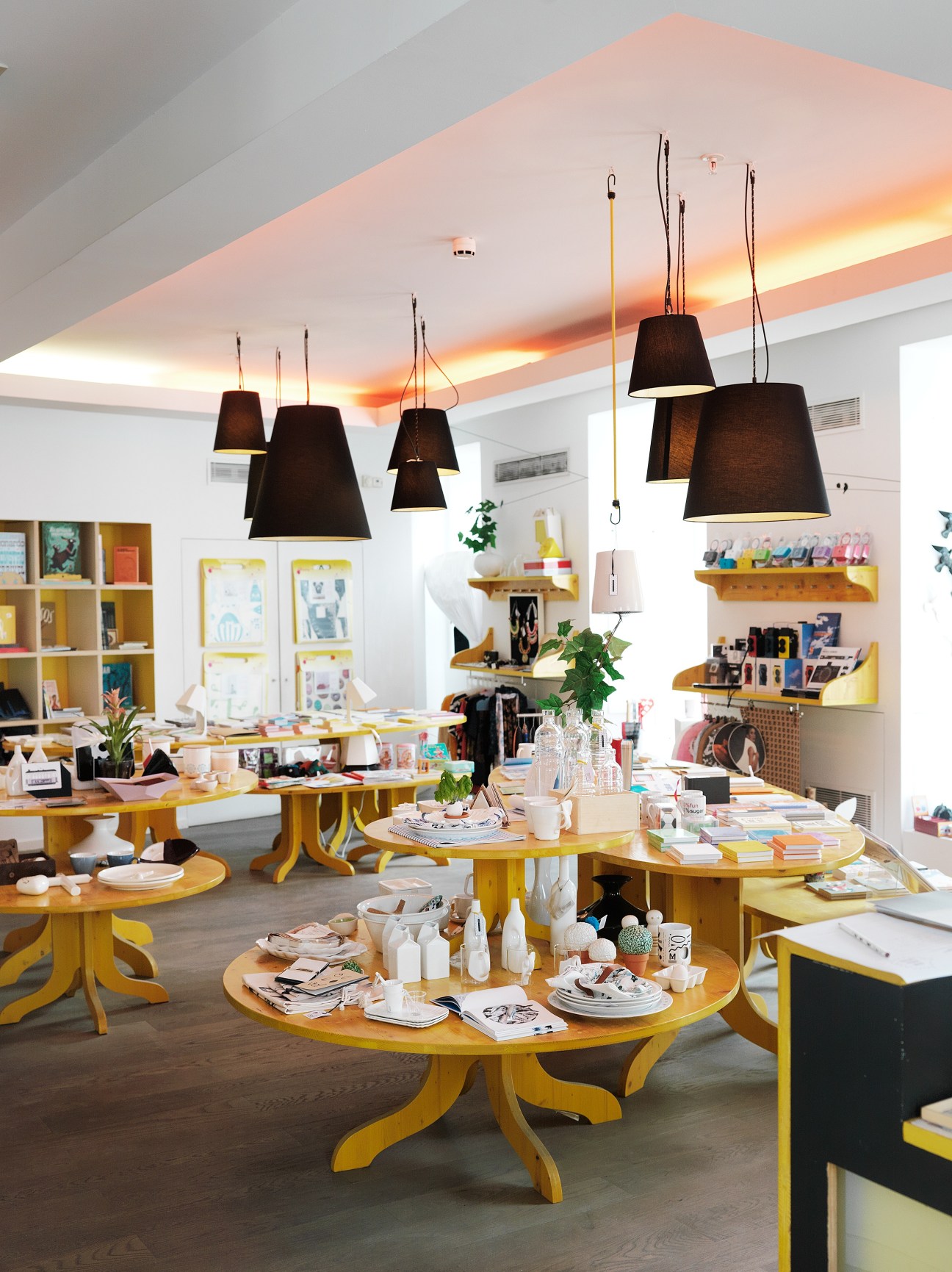 Bright interior of Fabrica Features shop with yellow tables, black pendant lamps, and shelving displaying design items and books.