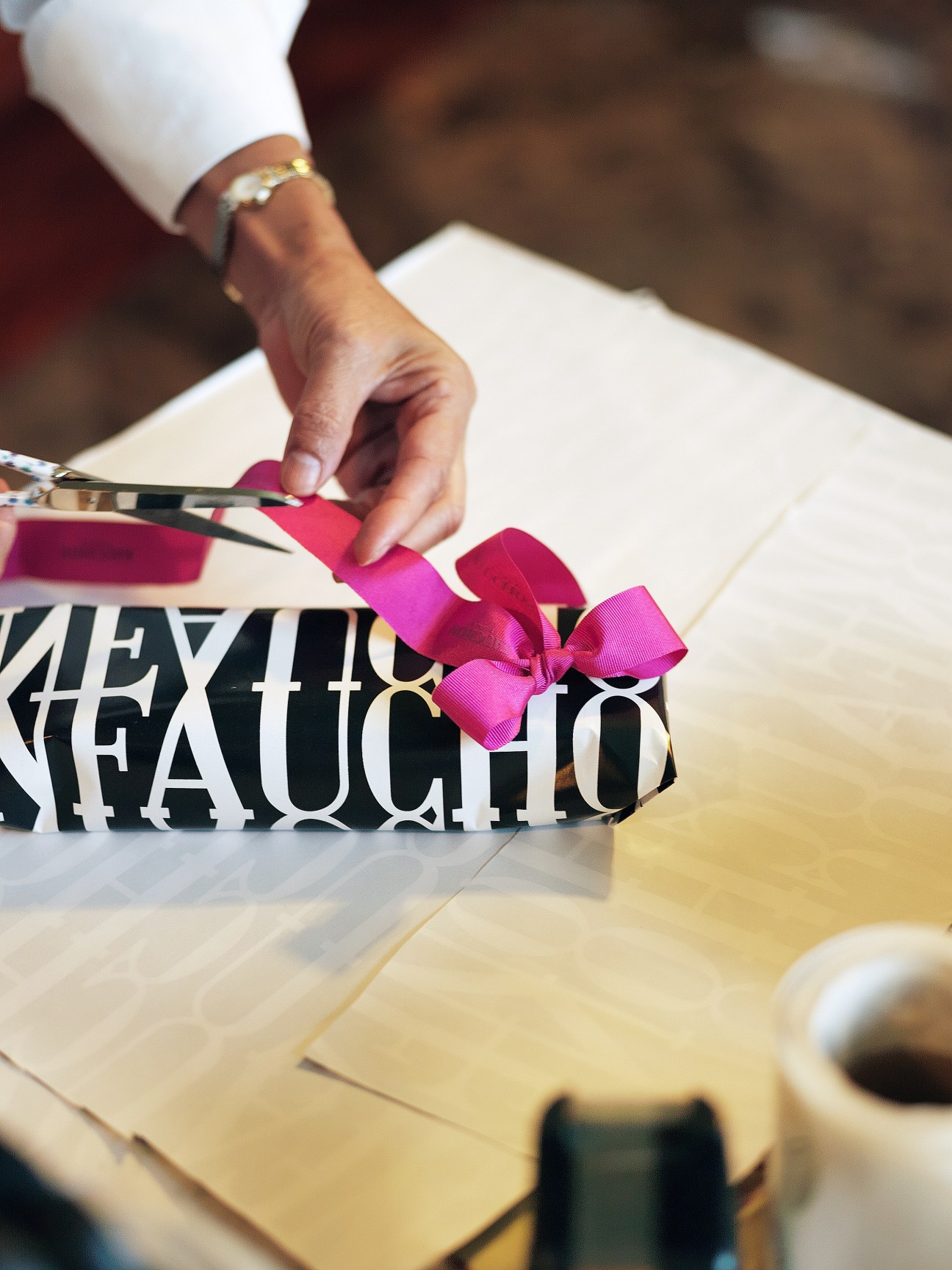 Person holding a wrapped gift with pink ribbon and black-and-white patterned paper at Charcutaria Moy.