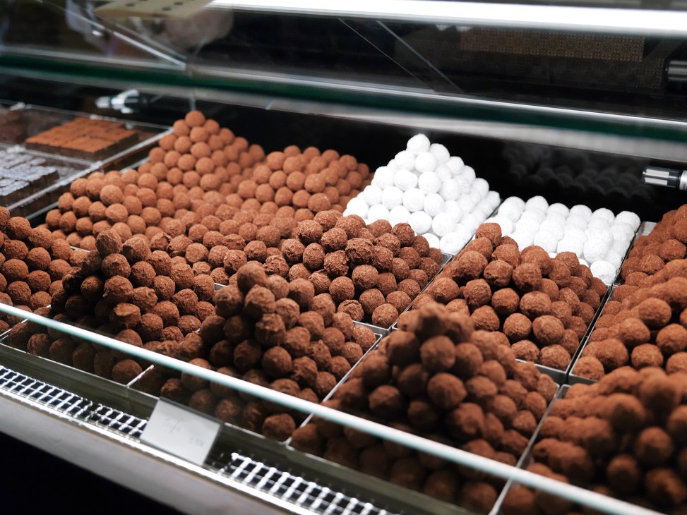 Display case of handmade chocolates and bonbons at Chocolataria Equador, including cocoa-dusted truffles and white-coated confections.