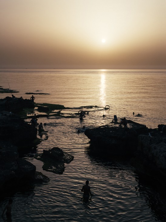 Silhouetted figure paddling in calm sea at sunset with golden light reflecting on water.