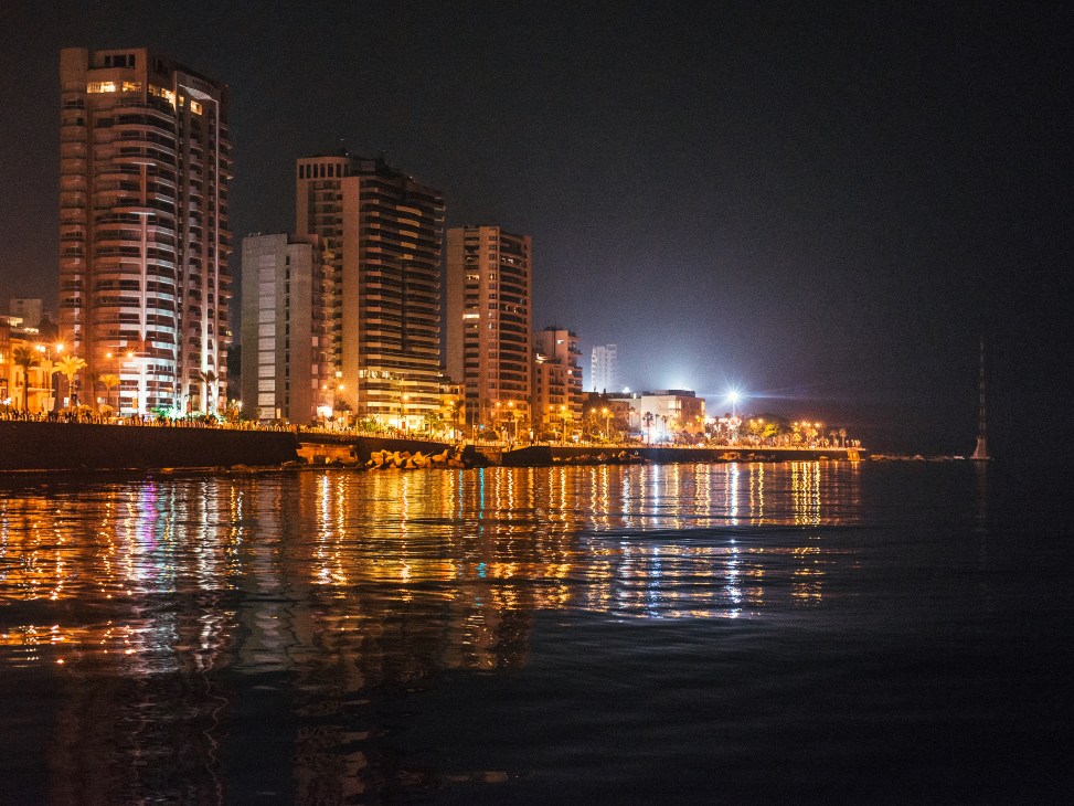 Beirut's illuminated waterfront at night with high-rise buildings reflecting in the Mediterranean Sea.