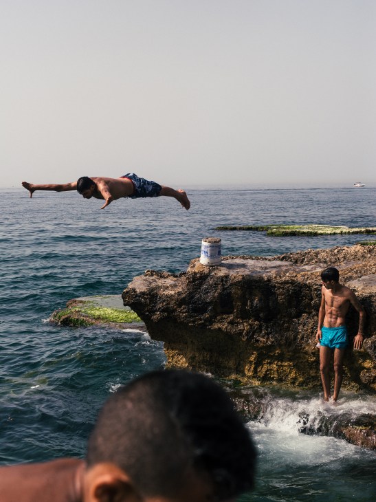 Men diving and swimming off rocky shore at American University of Beirut Beach in Beirut.