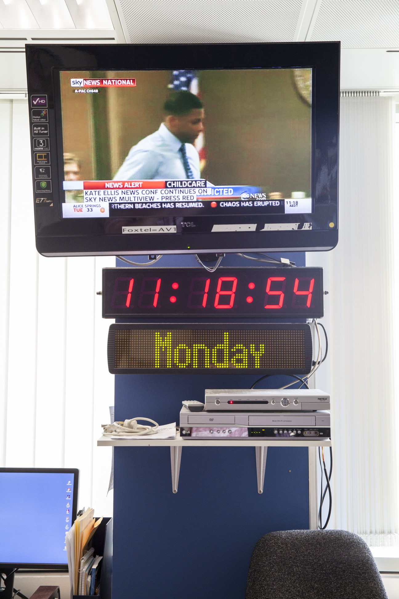 TV monitor displaying Sky News National broadcast mounted above digital clock and Monday indicator in newsroom.