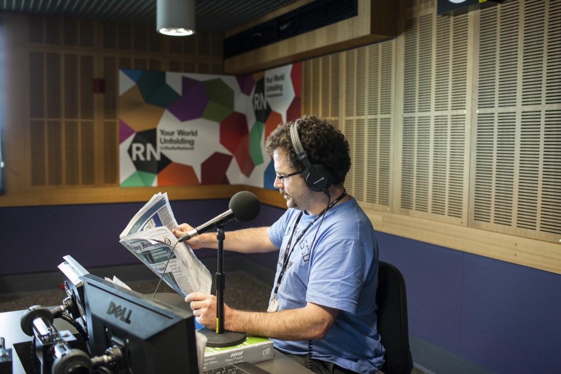 ABC Radio National reporter James Carleton reads the morning papers aloud into a microphone during broadcast.