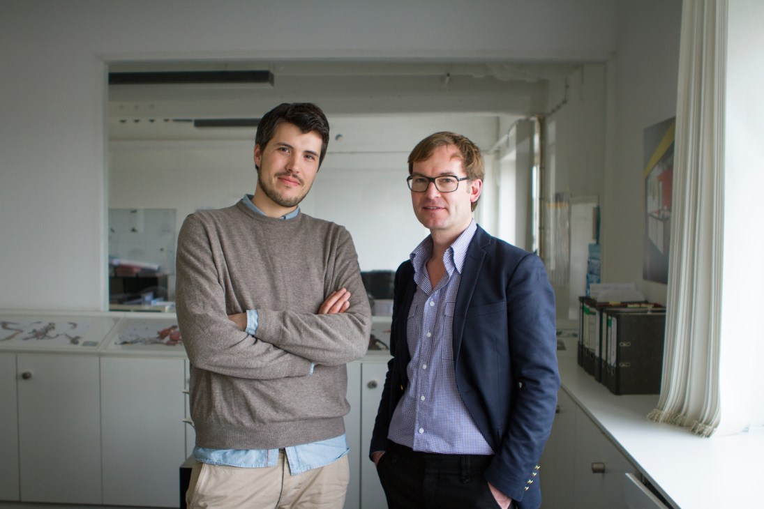 Xavier Busch and Gisbert Pöppler stand together in a modern interior space with white cabinetry and minimalist design.