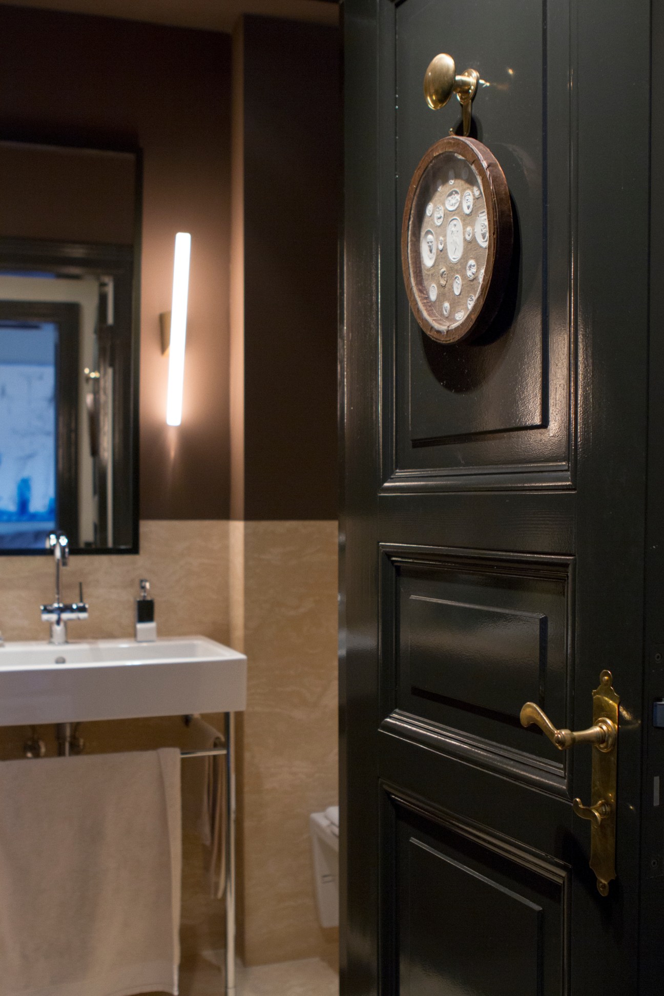 A modern bathroom with dark walls features a vintage clock in a wooden frame and a linear light fixture above a white sink.