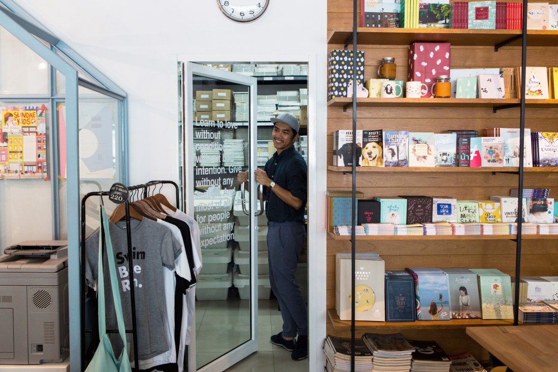 Man in cap standing in doorway of bookshop with wall-to-wall bookshelves filled with colorful volumes