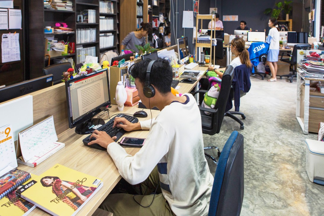 A Day department office with staff working at desks surrounded by magazines, plants, and bookshelves