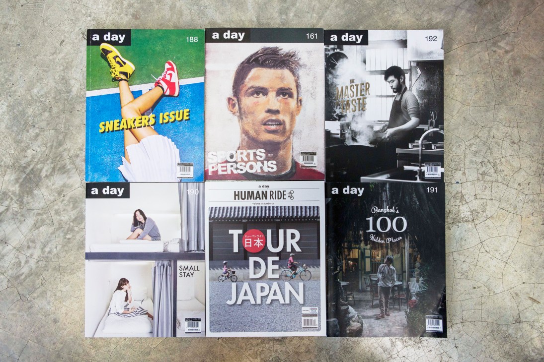 Collection of 'A Day' magazine issues laid out on concrete surface showing colorful covers with different themes