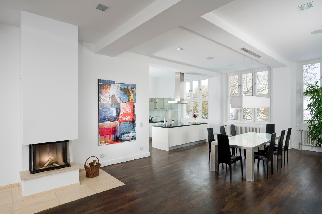 Modern loft interior with white walls, fireplace, dining area and open kitchen in Monroe Park Berlin.