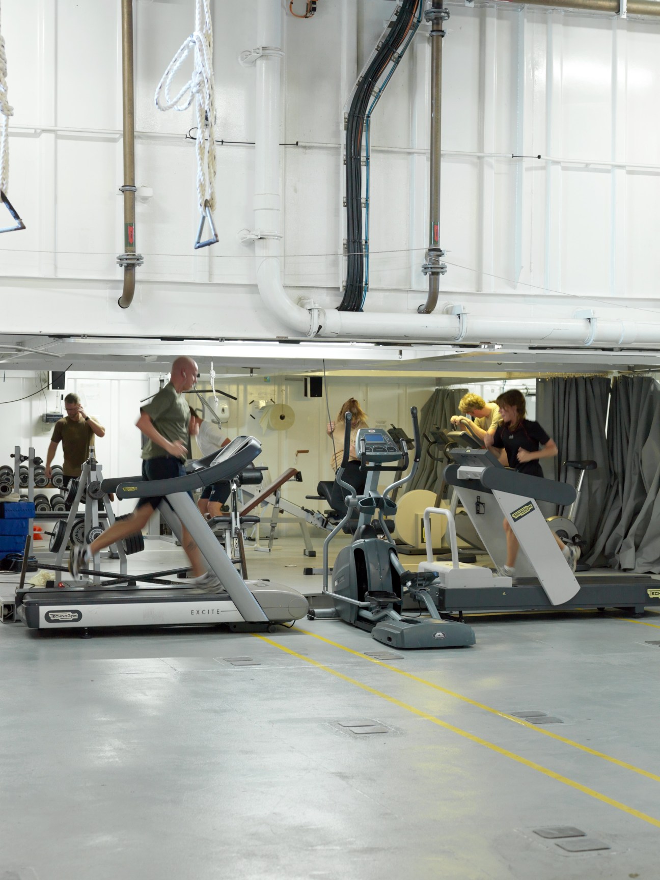 Crew members exercise on treadmills and other fitness equipment in the ship's gym.