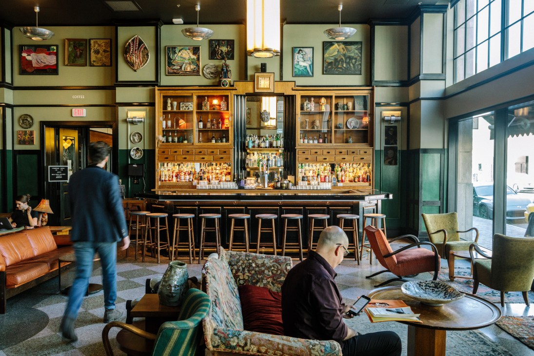 Main lobby of Ace Hotel New Orleans with bar, vintage furniture, and artwork on walls.