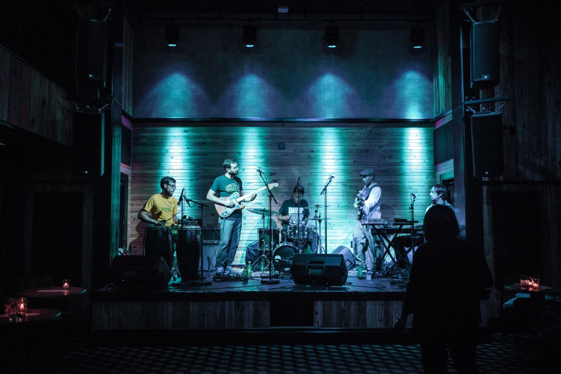 Local band BrasiNola performs on stage at Three Keys music venue inside Ace Hotel New Orleans, illuminated by blue lighting.