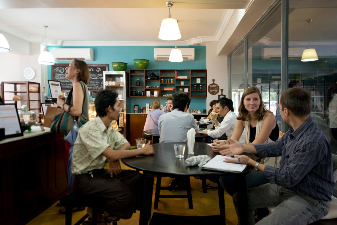 Interior of Yangon Bakehouse café with customers seated at tables and turquoise shelving displaying products.