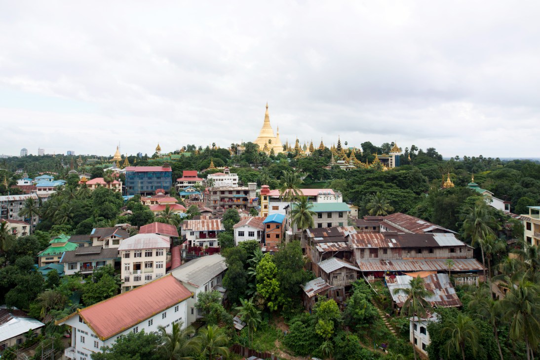 Shwedagon Pagoda with golden spires rises above residential buildings and palm trees in Yangon.