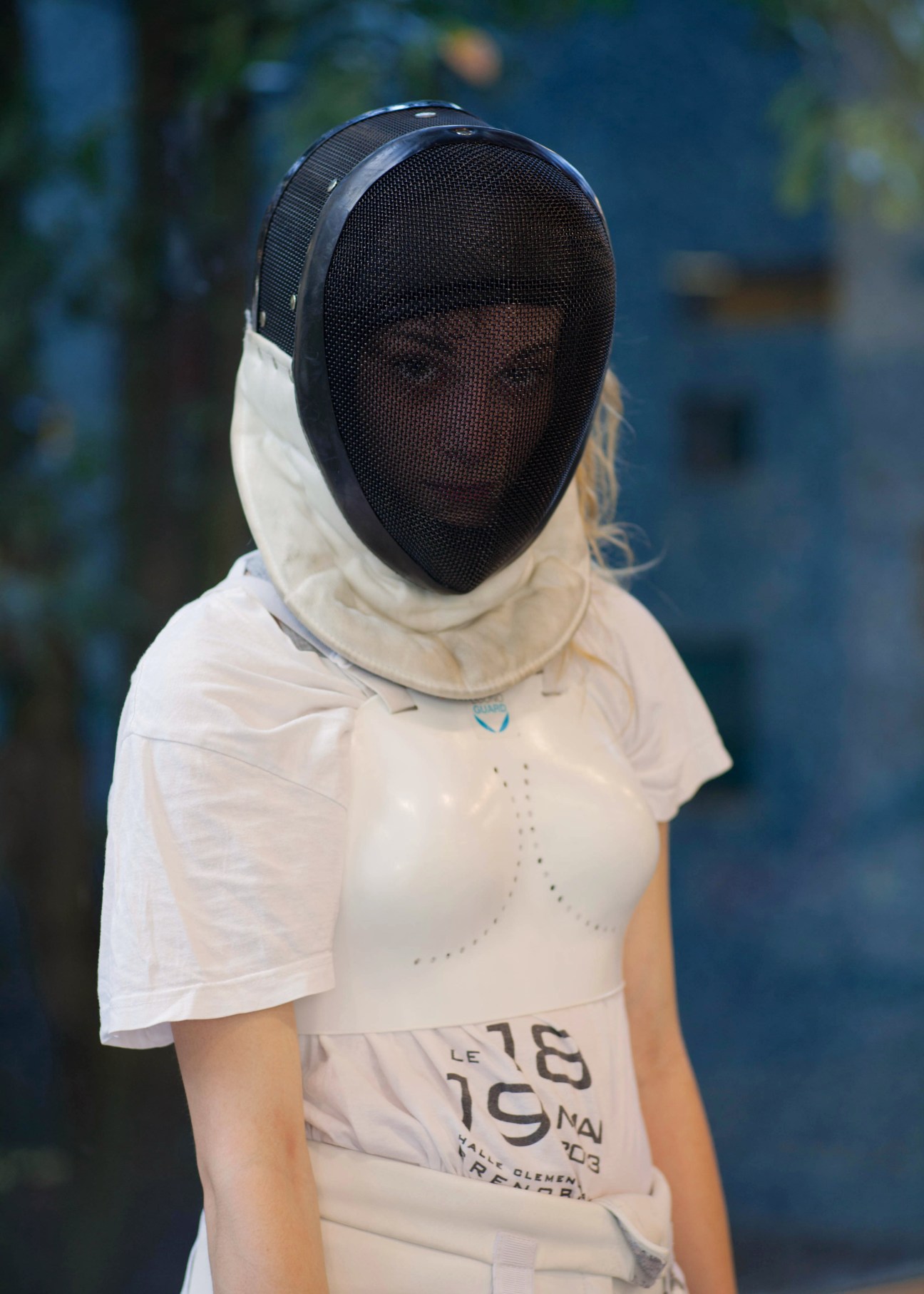 Fencer in white uniform wearing protective mesh mask and gear at Espace Sud sports facility.