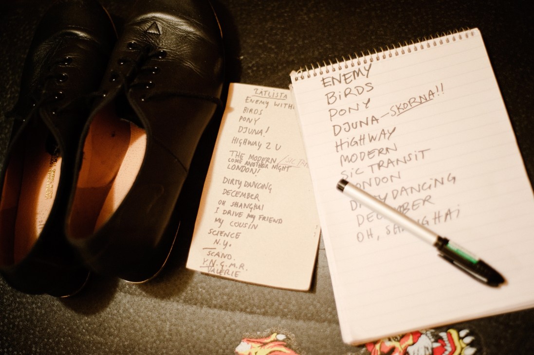 Handwritten setlist on spiral notebook pages next to headphones and a pen.
