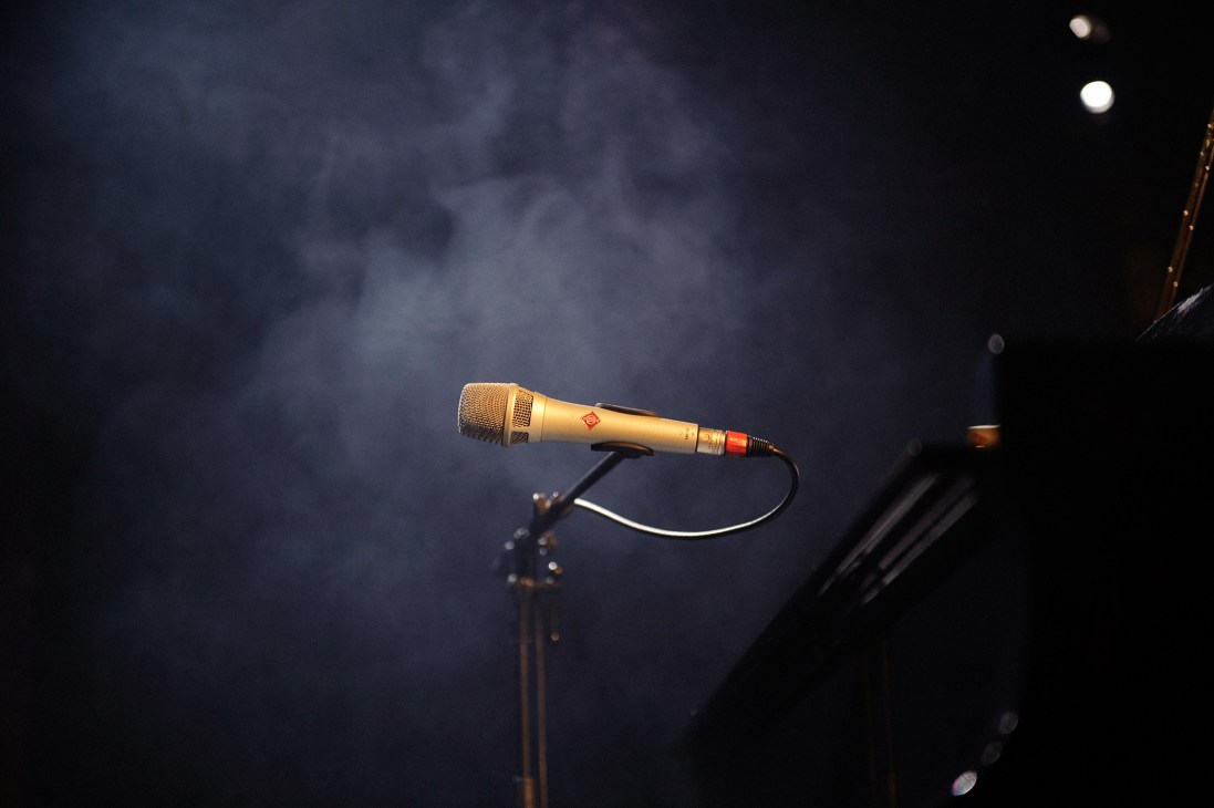 A gold microphone on a stand under stage lights with smoke in the background.