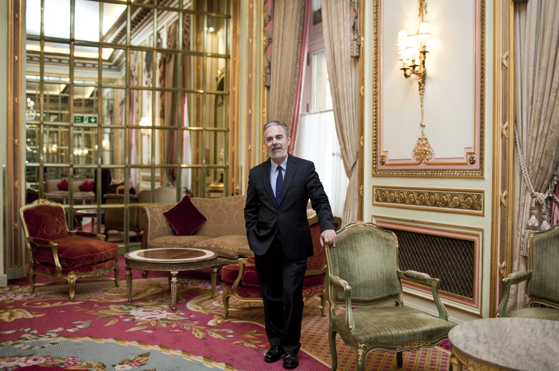 Antonio Patriota stands in an ornate hotel lounge with gold-framed mirrors and classical furnishings.