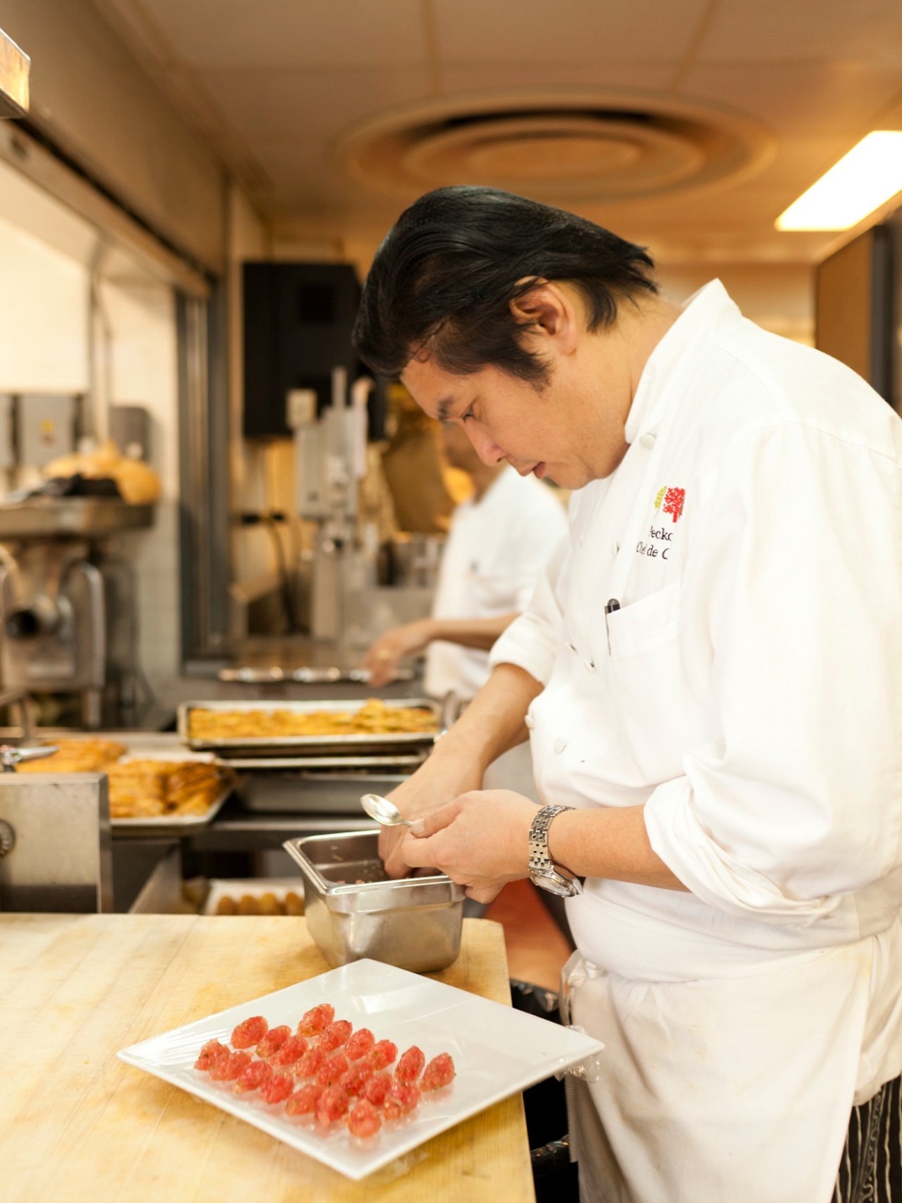 Sous chef in white chef's coat preparing nigiri sushi in kitchen.