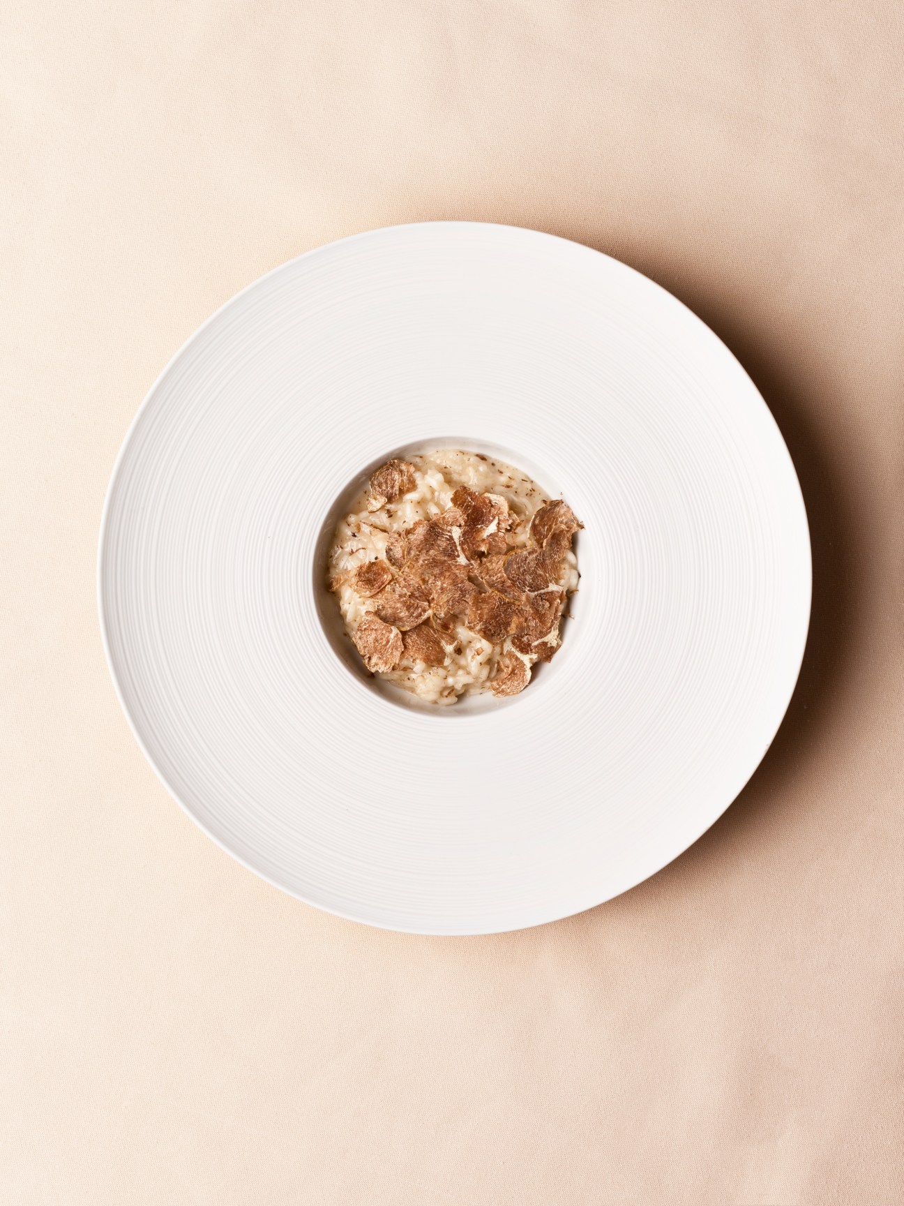 Risotto with white truffle shavings on a white plate against a beige background.