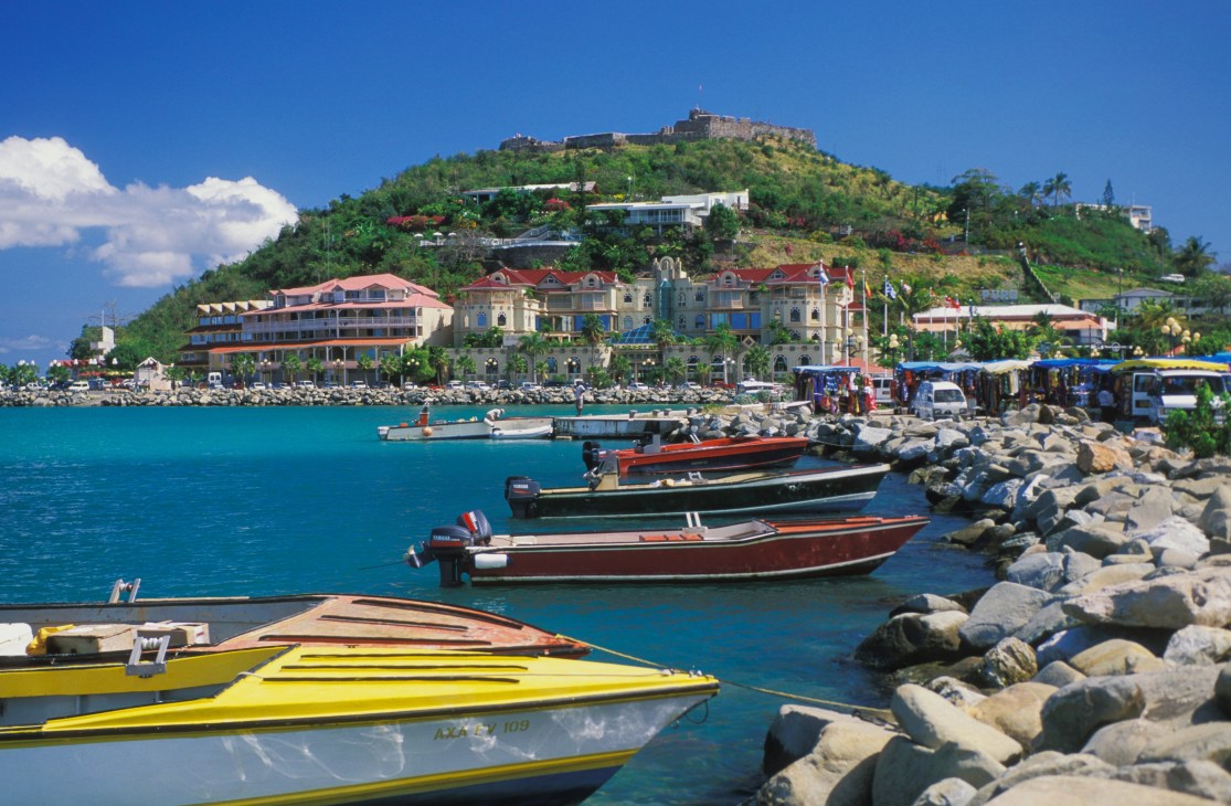 Colorful fishing boats moored in turquoise water with colonial buildings and lush hillside in Port Louis, Mauritius.