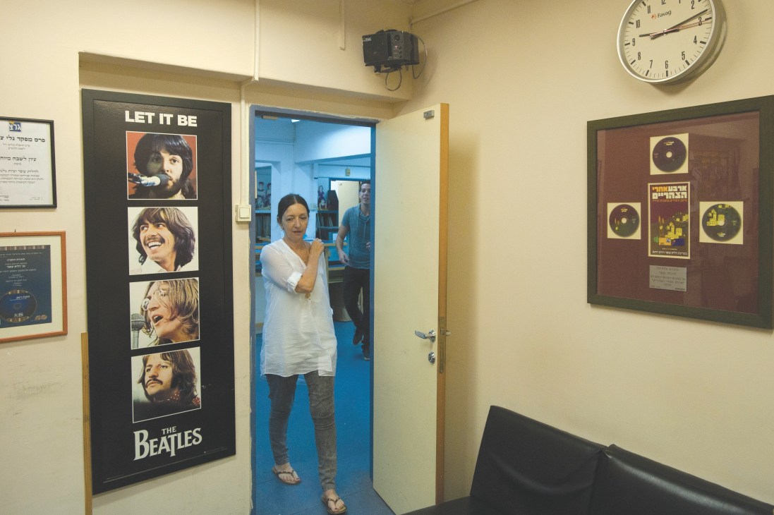 Dalit Ofer, manager of Galgalatz radio station, stands in a hallway with Beatles poster and music memorabilia.