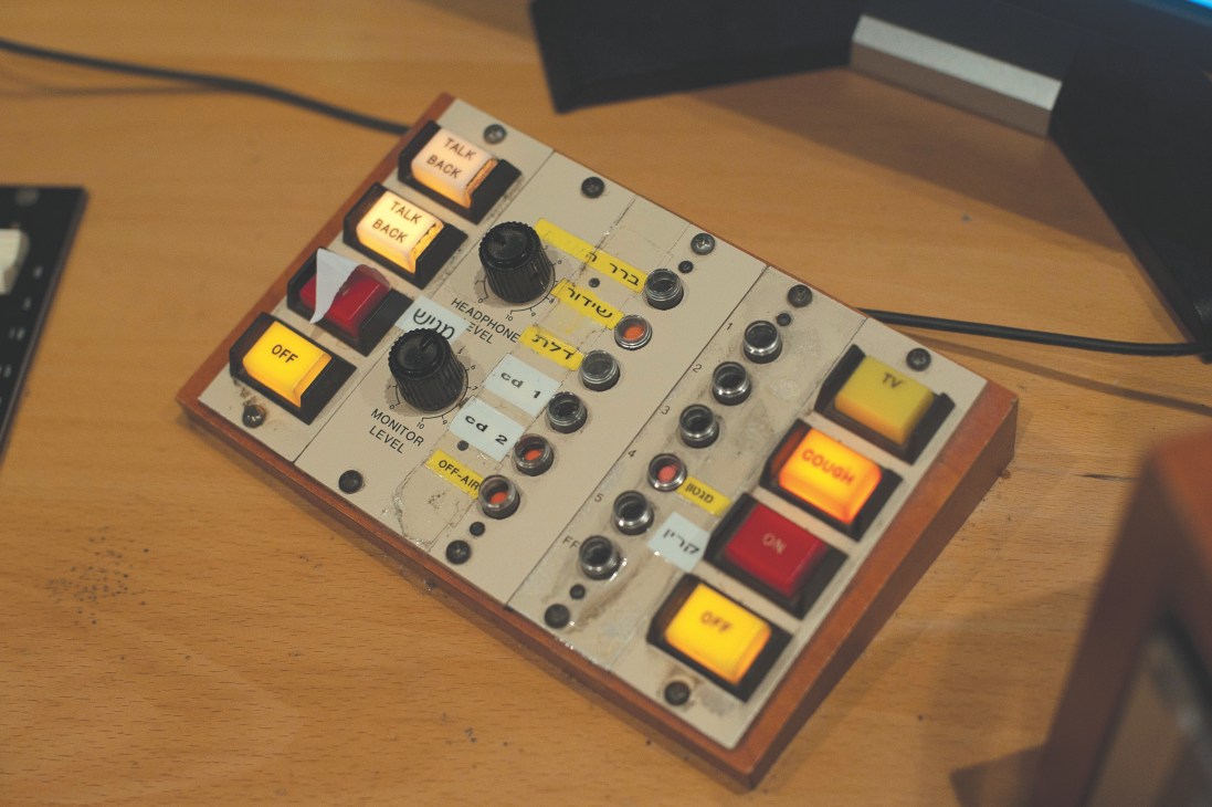 Audio mixing console with labeled buttons and dials in a radio station control room.