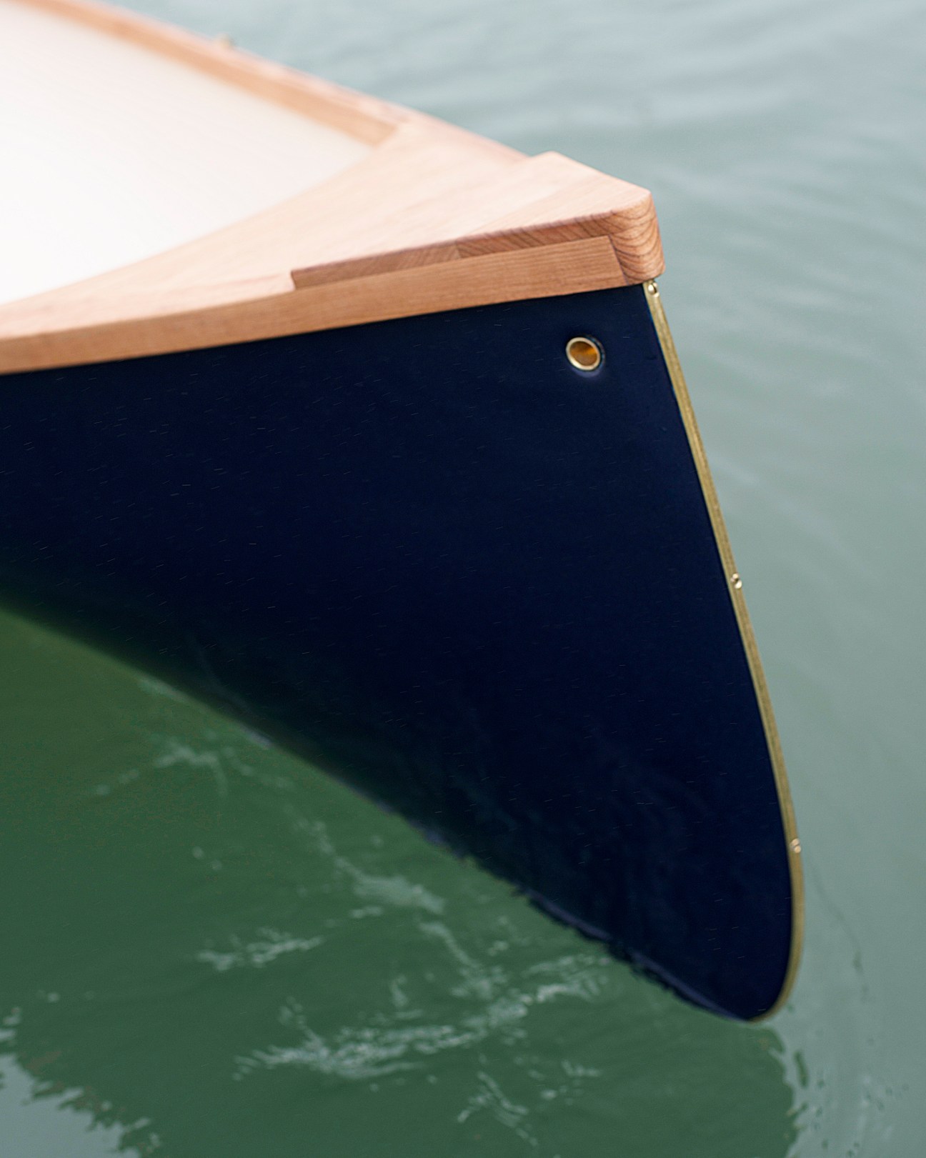 Close-up of a wooden rowboat edge showing oiled cherry wood construction with brass hardware.