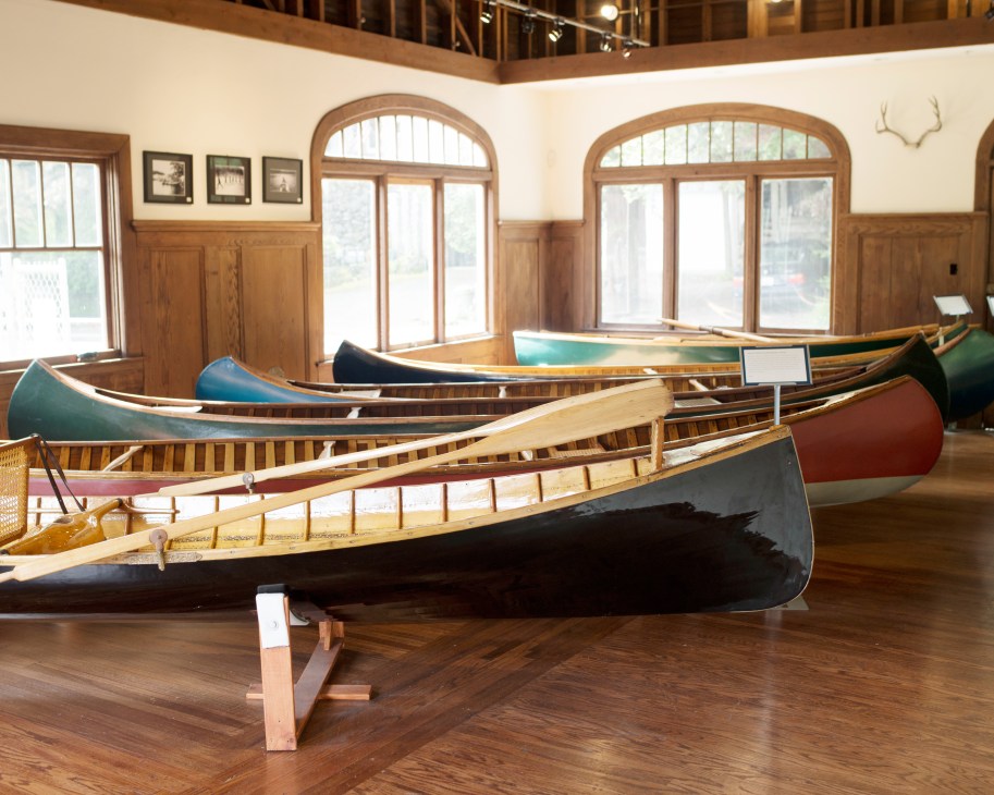 Multiple handcrafted rowboats displayed in a wooden-lined showroom with arched windows.