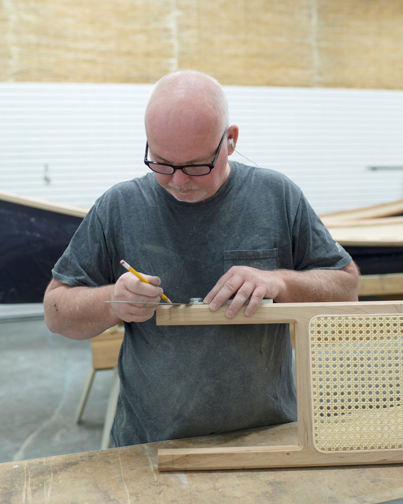Boatmaker carefully marking wood detail on boat frame in workshop.