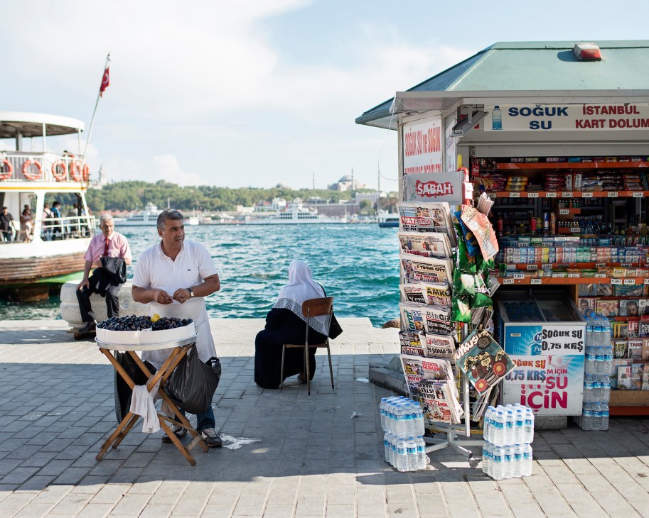 Man selling mussels at waterside kiosk displaying newspapers and magazines in Istanbul.