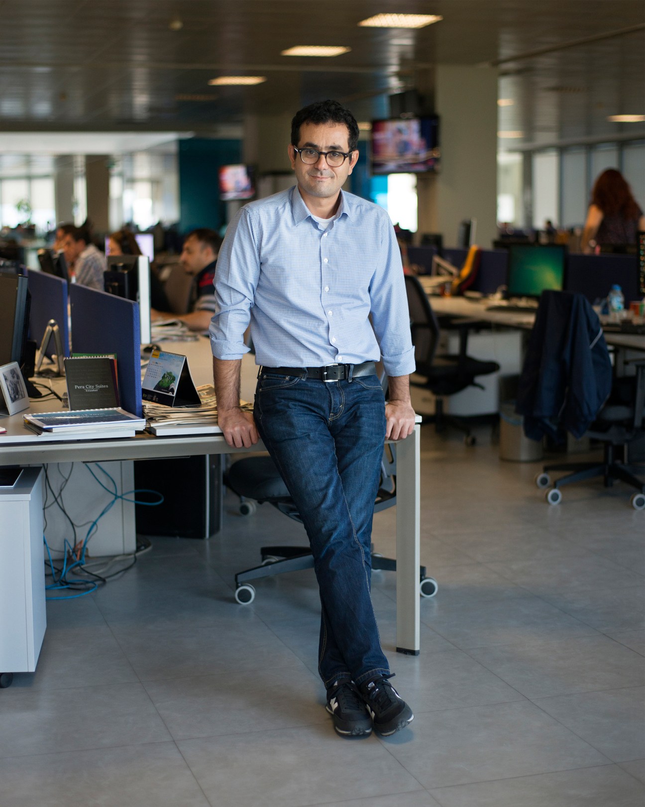 Cem Erciyes, weekend supplement editor for Radikal, standing at his desk in a newsroom office.