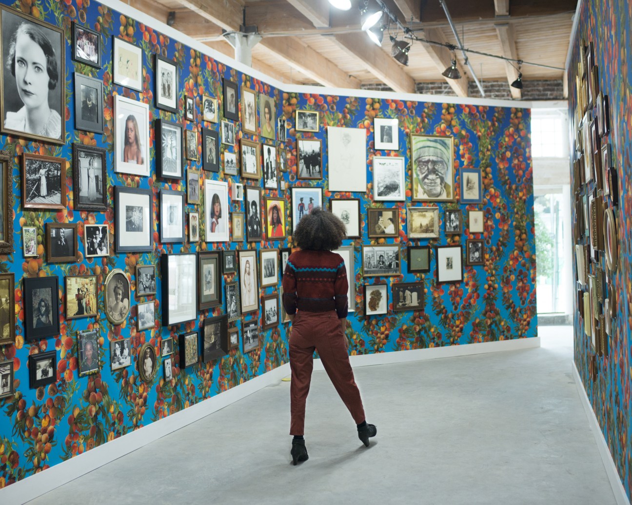 Visitor viewing a gallery wall covered with framed photographs and portraits on a vibrant blue and red patterned background.
