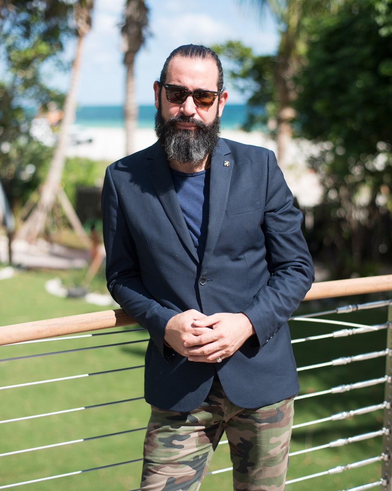 Josh Wagner standing by a modern railing with palm trees and beach visible behind him in Miami.